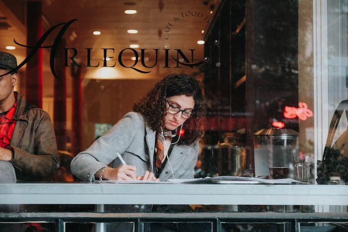 woman in cafe writing in journal Gratitude Journal